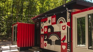 A cabin with a red exterior, a mural with various symbols, and outdoor seating. - The Buckeye Box - The James (McArthur)