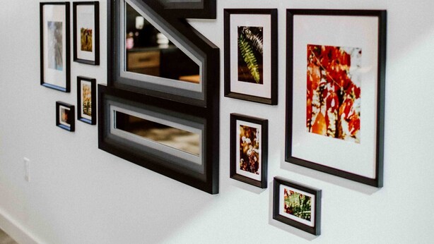 A wall with multiple framed pictures and a large black geometric structure. - The Buckeye Box - The James (McArthur)