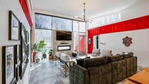 A modern living room with a large sofa, a dining table, and a TV. There are potted plants and a fireplace. - The Buckeye Box - The James (McArthur)