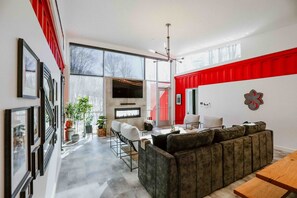 A modern living room with a large sofa, a dining table, and a TV. There are potted plants and a fireplace.