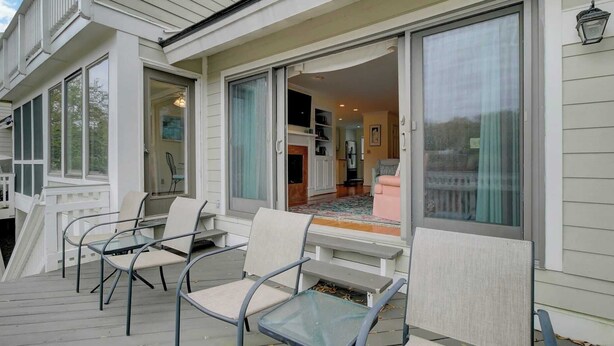 A covered porch with outdoor seating, a sliding glass door leading to an interior space with a kitchen and a living area. - 43 Fairway Dunes by Avantstay Coastal Charm + Golf! (Isle of Palms)
