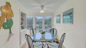 A dining area with a glass table, metal chairs, a ceiling fan, and a view of the outdoors. - 43 Fairway Dunes by Avantstay Coastal Charm + Golf! (Isle of Palms)