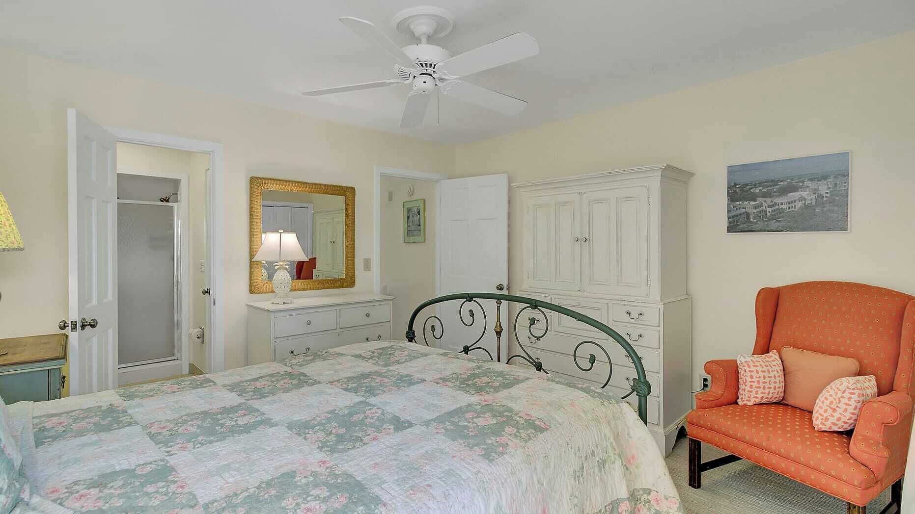 A bedroom with a bed, a chair, a wardrobe, a mirror, and a ceiling fan.