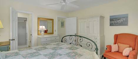 A bedroom with a bed, a chair, a wardrobe, a mirror, and a ceiling fan.