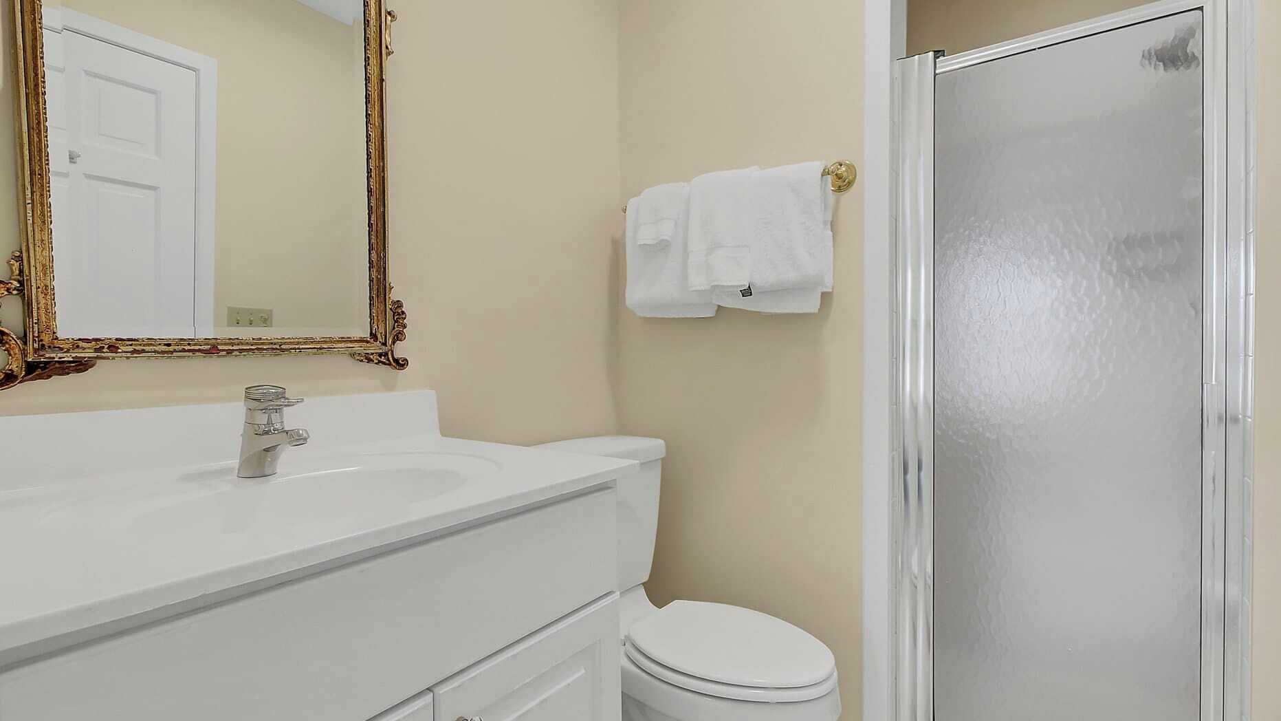Un bany amb un vàter blanc, un mirall amb una ornamentació elaborada, un lavabo i una cabina de dutxa de vidre.