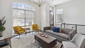 Ein modernes Wohnzimmer mit einer Couch, Sesseln, einem Couchtisch und großen Fenstern.