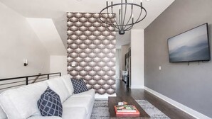 Una sala de estar moderna con un sofá, una mesa de centro con libros, una pared con estampado, una araña y un televisor montado en la pared.