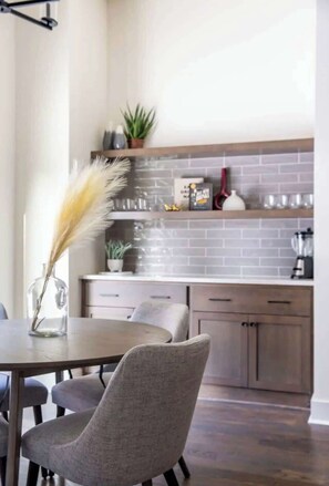 A modern kitchen with grey tiled backsplash, wooden cabinets, and a dining area with a table and chairs. - 2 West End Homes with Stunning Rooftop Views (Nashville)