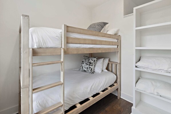 Una cama individual con ropa de cama blanca y un cojín estampado.