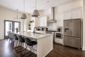 Une cuisine moderne dotée d’un îlot central, d’appareils électroménagers en acier inoxydable et de luminaires suspendus.
