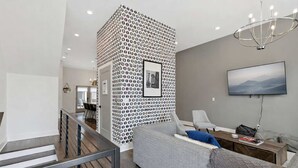 Una sala moderna con un sofá gris, un televisor y una pared estampada.