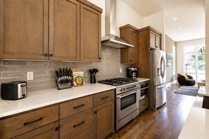 A modern kitchen with wooden cabinets, a gas stove, a stainless steel refrigerator, and a toaster.