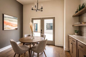 A dining area with a round table, four chairs, a chandelier, and a view through a glass door to the outside. - Stylish West End Stay with Rooftop & Patio (Nashville)