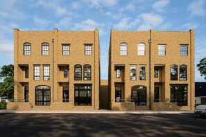 Un edificio de ladrillo de dos pisos con ventanas y puertas simétricas, techo plano y suelo pavimentado.