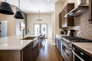 A modern kitchen with a central island, stainless steel appliances, and a view to the dining area. - Stylish West End Stay with Rooftop & Patio (Nashville)