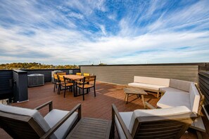 Una terraza en la azotea con una mesa y sillas de madera, un sofá y un equipo de aire acondicionado.