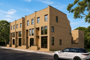 A multi-story building with a brick facade, large windows, and a white car parked in front. - Stylish West End Stay with Rooftop & Patio (Nashville)