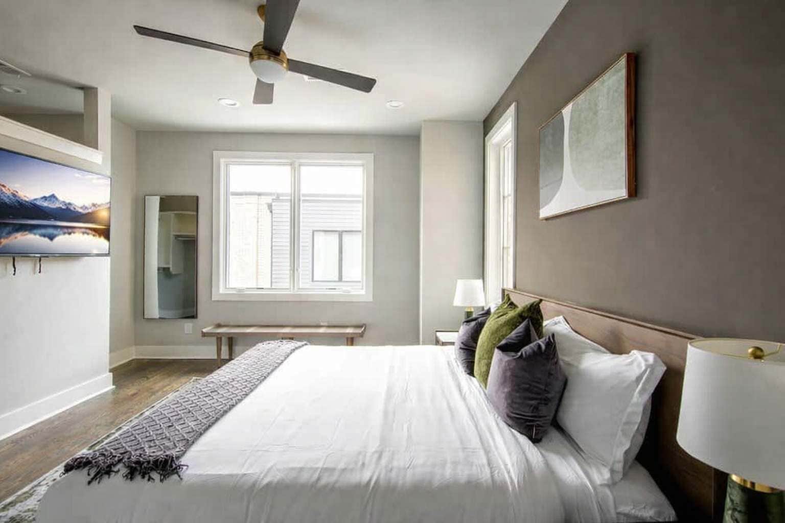 Una camera da letto con un letto, una ventola a soffitto, una finestra, una panchina e un quadro.