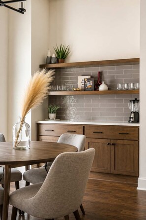 Une cuisine moderne avec une table à manger en bois, des chaises et une étagère intégrée où sont exposés des objets décoratifs.