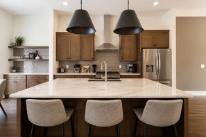 A modern kitchen with a large island, bar stools, wooden cabinets, and stainless steel appliances.