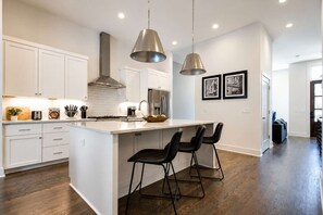 A modern kitchen with white cabinetry, a central island with bar stools, stainless steel appliances, and pendant lighting.
