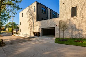 Un edificio moderno con entrada de garaje, un camino de entrada pavimentado y un árbol pequeño al frente.