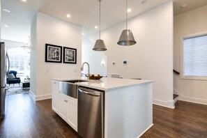A modern kitchen with a central island, stainless steel appliances, pendant lighting, and a view of the living area.