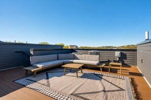 Una terraza en la azotea con un sofá modular, una mesa de madera y un tapete estampado.