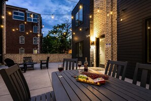 Eine Terrasse im Freien mit Esstisch, Stühlen und einer Lichterkette darüber.