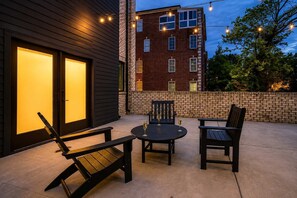 An outdoor patio with a table and chairs, a brick wall, and a building with lit windows in the background.