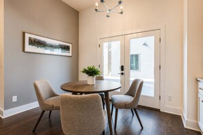 A dining area with a round table, four chairs, a potted plant, and a chandelier.