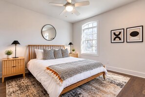 Ein Schlafzimmer mit Bett, Nachttischen, Deckenventilator, Fenster und Wandbildern.