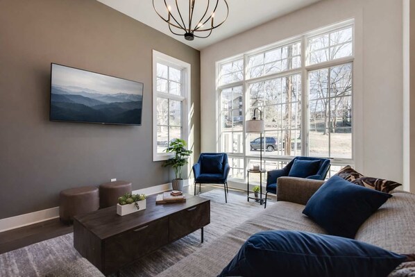 A living room with a large window, a mounted TV, a coffee table, and two sofas.