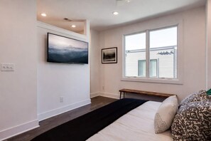 A bedroom with a bed, a bench, a window, and artwork on the wall.