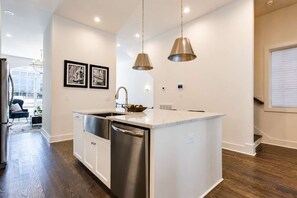 Une cuisine moderne dotée d’un îlot central, d’appareils électroménagers en acier inoxydable, de luminaires suspendus et donnant sur un espace repas.
