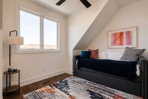 A bedroom with a sloped ceiling, a bed with multiple pillows, a floor lamp, a rug, and a painting on the wall.