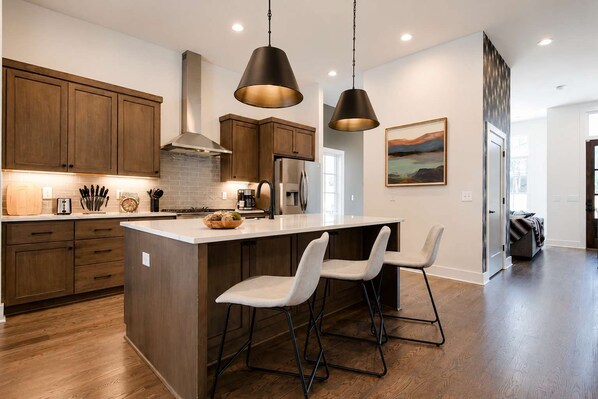 A modern kitchen with wooden cabinets, a central island with bar stools, and pendant lighting.