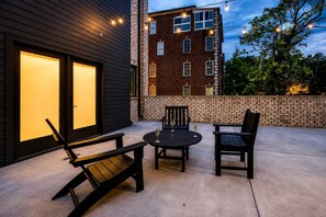 Une terrasse extérieure avec une table ronde et deux chaises, un mur de briques et un bâtiment doté de grandes fenêtres.