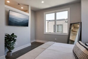 A bedroom with a bed, a window, a plant, and a painting on the wall. - New Build West End Oasis • Skyline Views (Nashville)