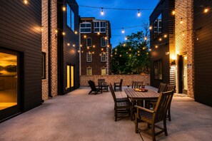 An outdoor patio area with a brick wall, wooden tables, and chairs, and string lights. - New Build West End Oasis • Skyline Views (Nashville)