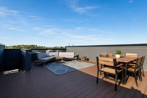 Una terraza en la azotea con un sofá, una mesa, sillas y una planta en maceta.