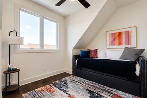 A bedroom with a sloped ceiling, a large window, a bed with multiple pillows, a floor lamp, and a patterned rug. - New Build West End Oasis • Skyline Views (Nashville)