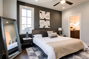 A bedroom with a large bed, a nightstand, a mirror, a ceiling fan, and a window. - New Build West End Oasis • Skyline Views (Nashville)