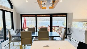 Un comedor moderno con una mesa grande y sillas, ventanas amplias con vista al lago, y un techo con vigas a la vista e iluminación.