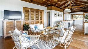 A room with wicker furniture, a television, and a kitchen area. - Stu’s Lookout - Stunning Views (Wongaling Beach)