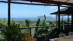 A terrace with a view of the ocean and a mountain, featuring outdoor seating and potted plants. - Stu’s Lookout - Stunning Views (Wongaling Beach)