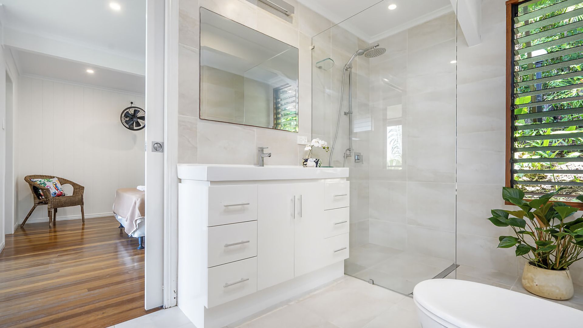 A modern bathroom with a glass shower enclosure, a white vanity with drawers, and a potted plant.