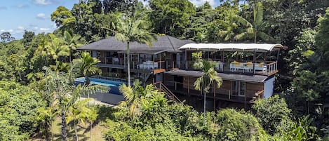 A two-story house with a pool, surrounded by dense tropical vegetation.