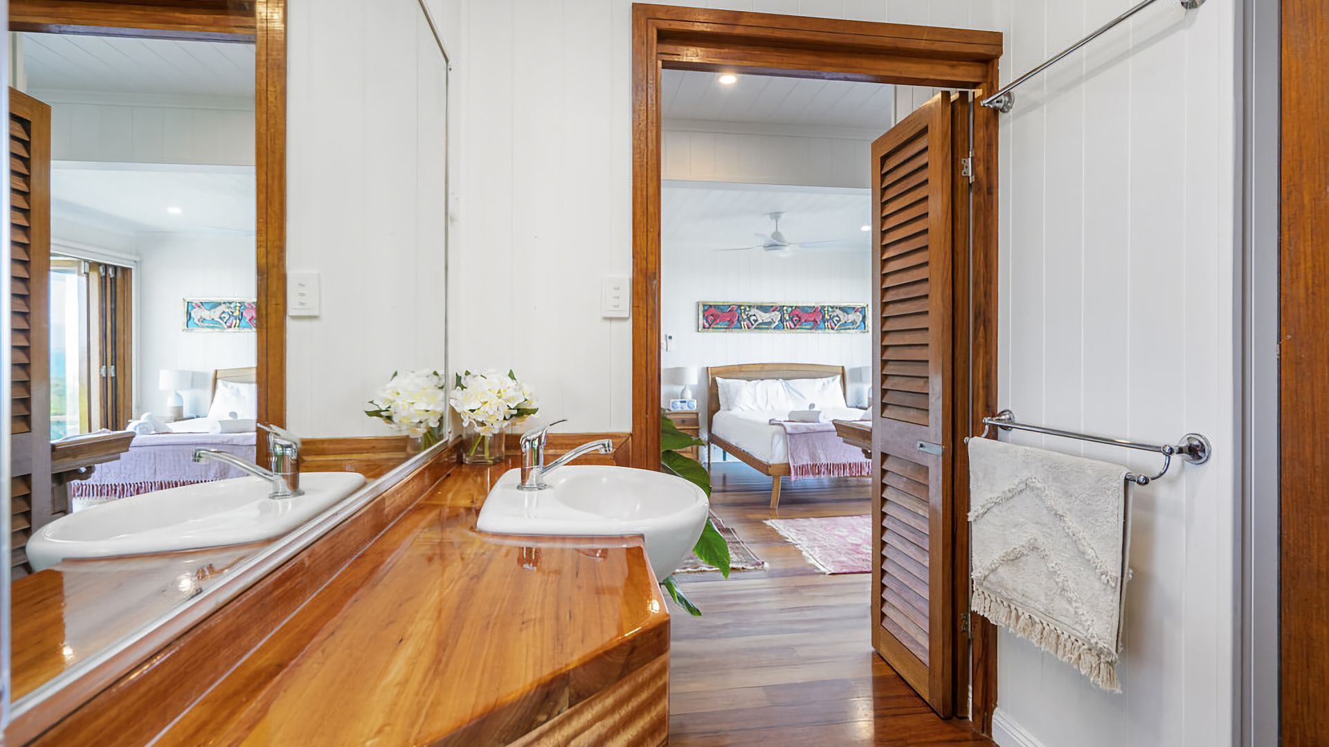 A bathroom with wooden flooring, two sinks, a large mirror, and a towel rack.