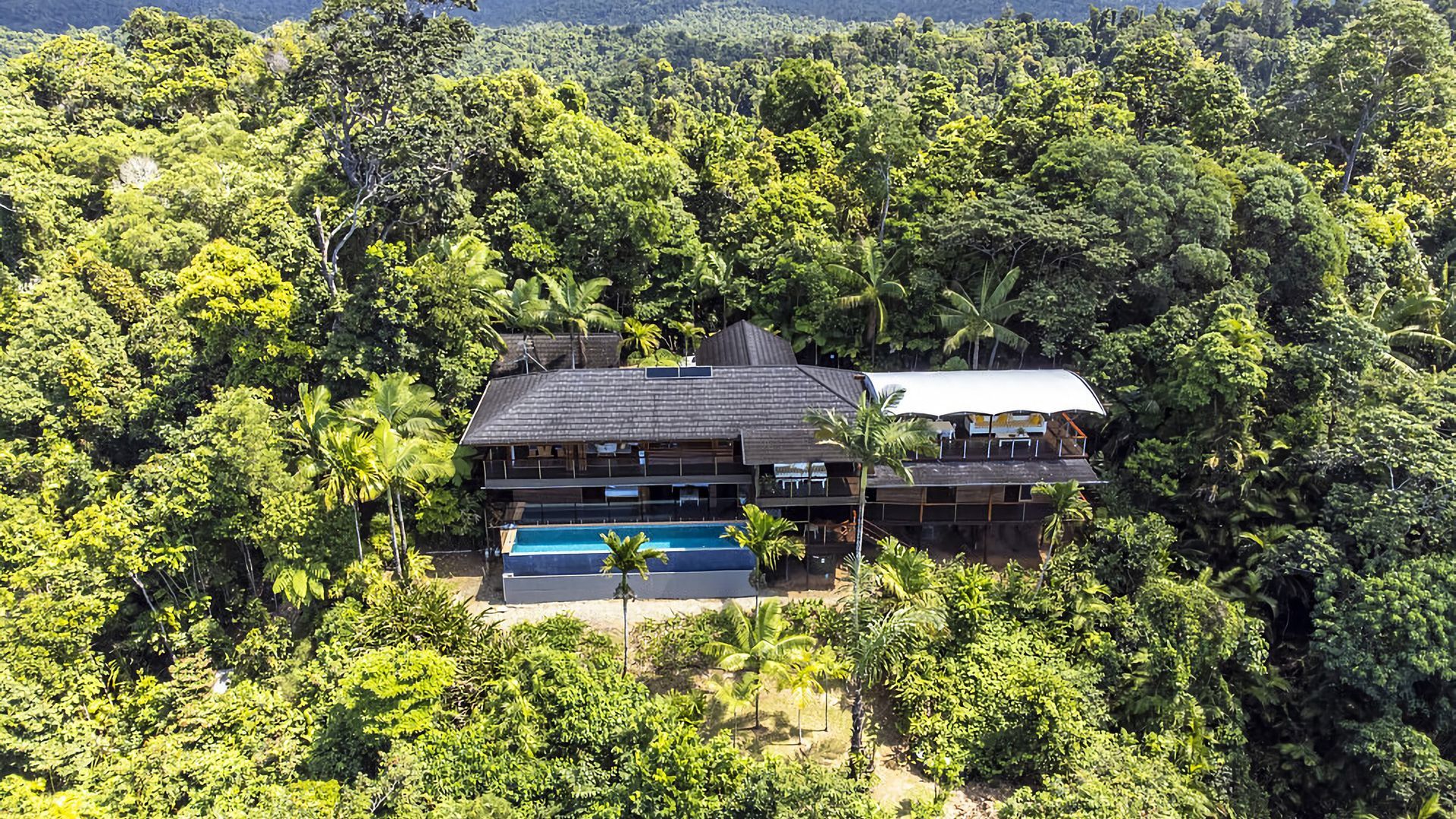 Una casa de dos pisos con piscina rodeada de exuberante vegetación tropical.